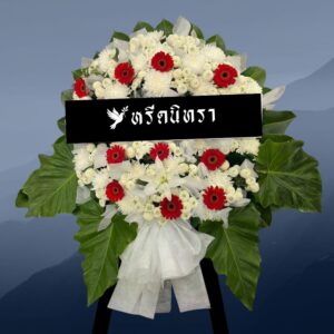 พวงหรีดดอกไม้สดโทนสีขาวแดง ดีไซน์สุภาพโดดเด่น ตกแต่งด้วยดอกเยอบีร่าสีแดง ลิลลี่ และเบญจมาศ พร้อมใบไม้สีเขียวขนาดใหญ่