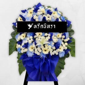 พวงหรีดดอกไม้สดโทนสีน้ำเงินขาว ดีไซน์เรียบหรู ตกแต่งด้วยดอกเยอบีร่า เบญจมาศ ลิลลี่ และดอกมัม พร้อมกระดาษสีน้ำเงินเข้ม ดูสุภาพและสง่างาม